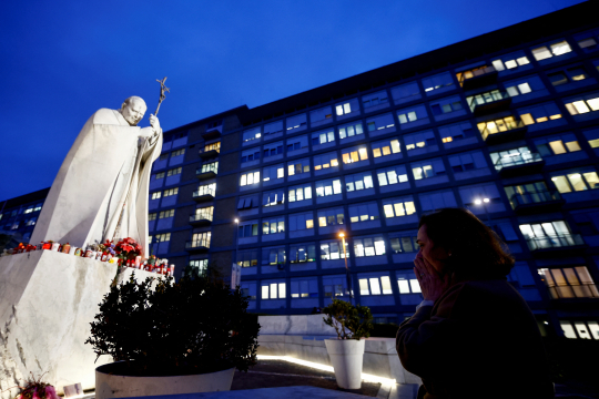 En kvinne ber foran statuen av pave Johannes Paul II utenfor Gemelli-sykehuset i Roma
