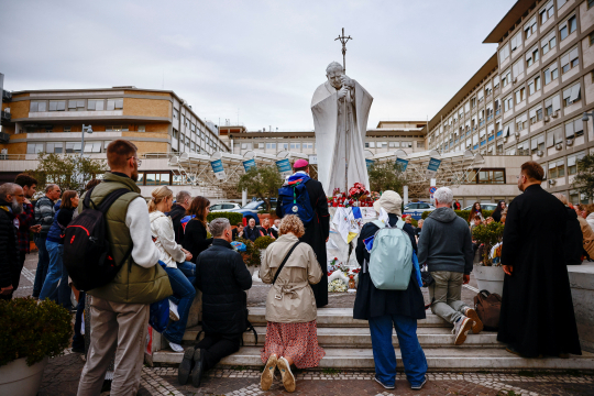 Biskop og troende ber rosenkransen foran Johannes Paul II-statuen utenfor Gemelli-sykehuset i Roma