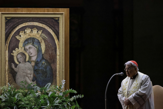 En kardinal ber foran et ikon av Jomfru Maria og Jesus på Petersplassen om kvelden