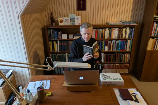 En prest leser en bok ved skrivebordet på kontoret sitt