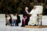 Pave Frans sitter i sin stol i Paul VI-salen, ved siden av to mødre som holder sine barn
