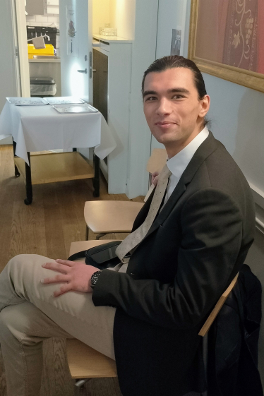 En ung mann sitter på en stol i menighetssalen i Akersveien og smiler mot kamera