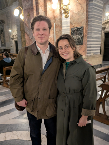 Et ungt par, en mann og en kvinne, står sammen i en kirke og smiler mot kamera