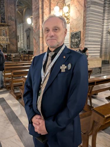 En eldre mann i dress står i en kirke i Roma og smiler mot kamera