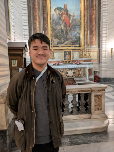 En ung mann står foran Olavsalteret i en kirke og smiler mot kamera
