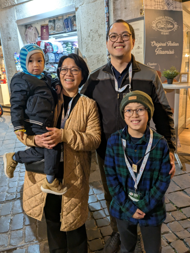 En familie med mor, far og to barn står på en gate i Roma og smiler til kamera