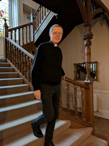 En prest går på vei ned en trapp og smiler mot kamera