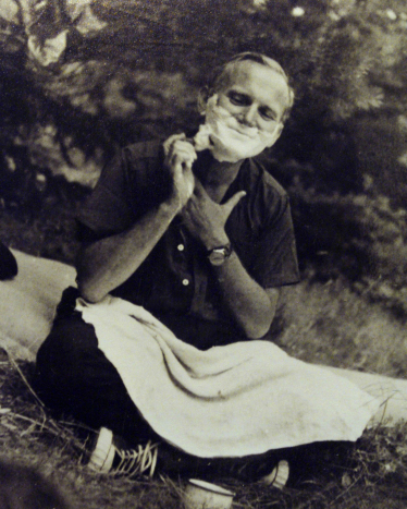 En ung Karol Wojtyla, kledd uformelt, sitter på gresset og barberer seg