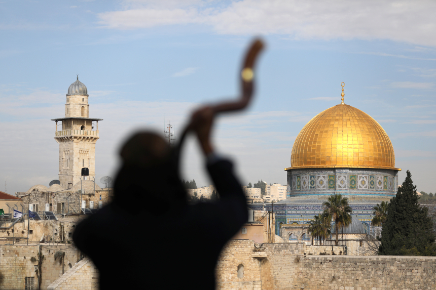 Mann sett i silhuett bakfra blåser i bukkehorn i Jerusalem