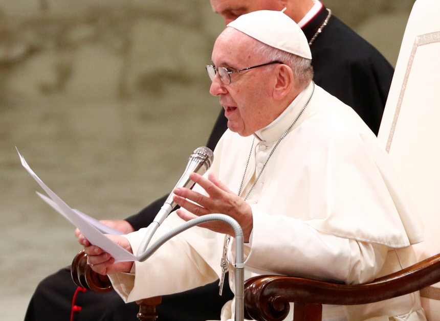 Pave Frans sitter på en stol og leser fra et dokument i Paul VI-hallen