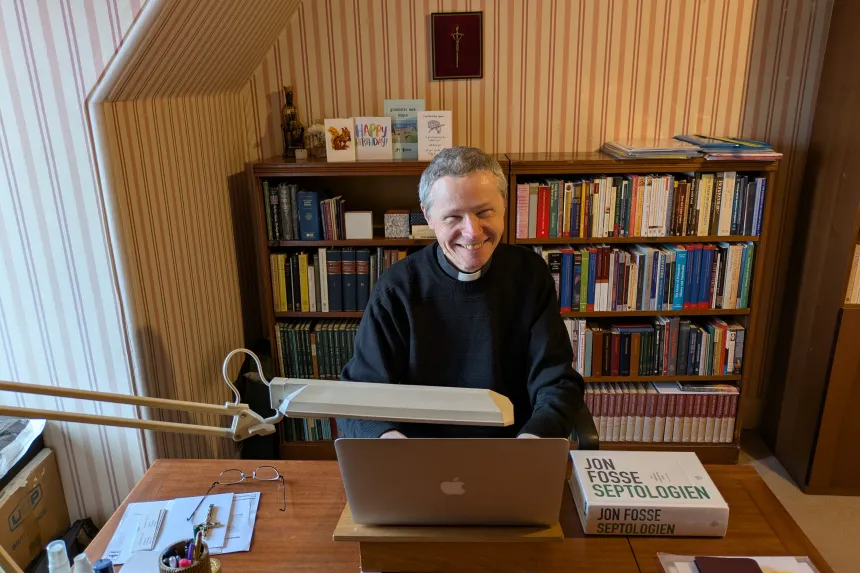 En prest sitter foran en laptop ved skrivebordet på kontoret sitt