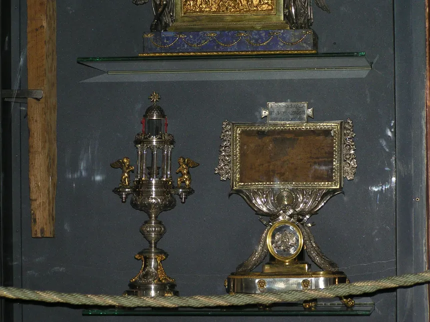 En treplate med inskripsjon i et relikvarium, ved siden av et annet relikvarium, i en glassmonter