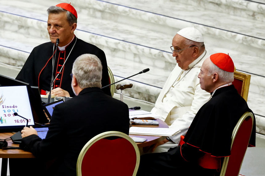 Pave Frans sitter ved et rundt bord med to kardinaler og andre i Paul VI-hallen