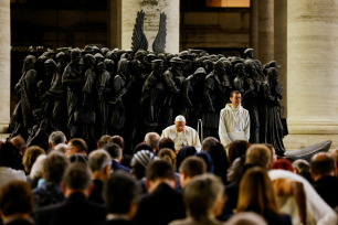 Pave Frans ber foran en statue av migranter på Petersplassen; foran ham står en folkemengde